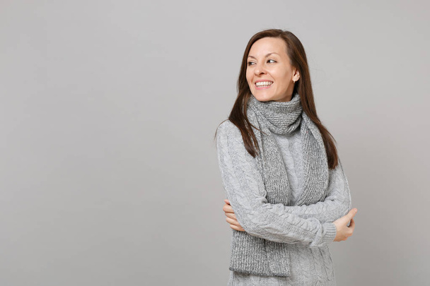 Улыбающаяся молодая женщина в сером свитере, шарф, держась за руки сложенными
  - Фото, изображение