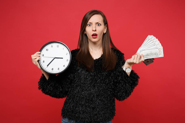Bewildered young woman in black fur sweater holding round clock  - Foto, Bild