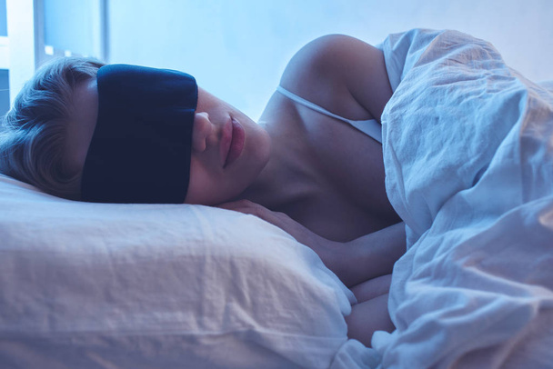 Sleeping girl in a sleep mask on an orthopedic pillow with night lighting, white bed linen. - Foto, imagen