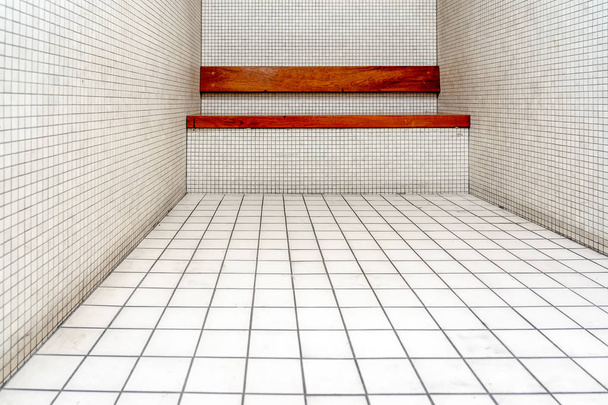 O interior muito sóbrio de uma cela de prisão: paredes de azulejos nuas e um banco de madeira
. - Foto, Imagem