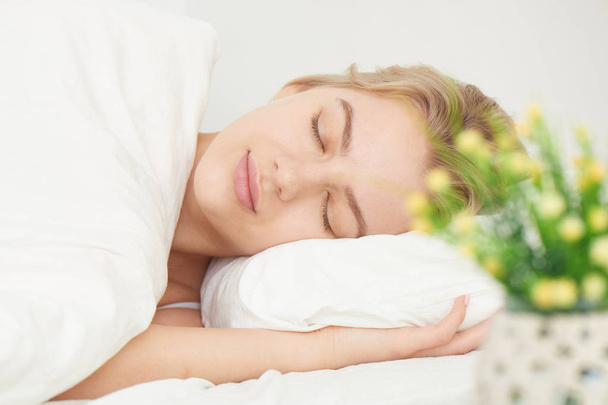 Nukkuva hymyilevä kaunis tyttö ortopedinen tyyny päivänvalossa, valkoiset lakanat ja kodin sisustus
 - Valokuva, kuva