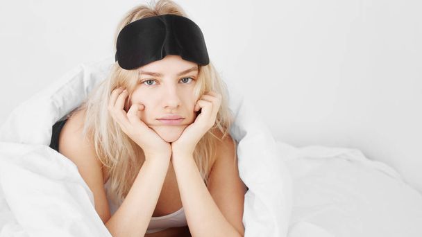 Concept of female health, insomnia, hangover, menstruation or feeling unwell in the morning. Young beautiful woman with displeased facial expression on white bed. - Photo, Image
