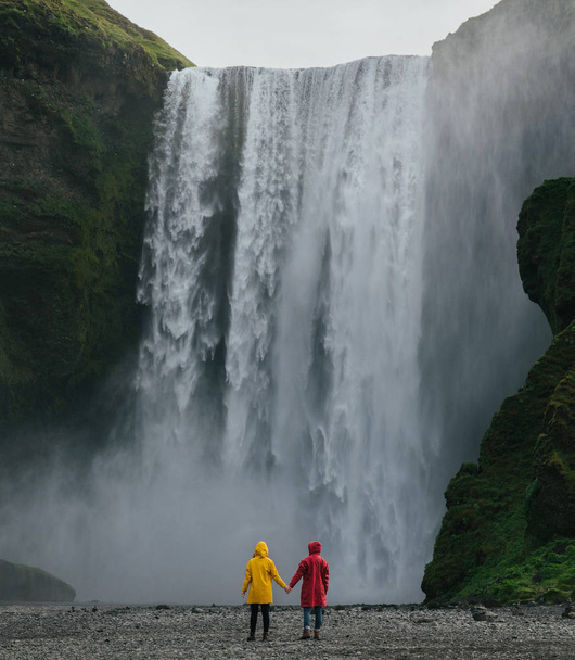 Couple in raincoats looking on scenic high waterfall - Фото, изображение