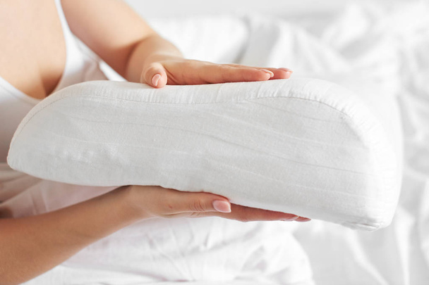Female hands hold and show an orthopedic pillow on a white bed. Comfortable sleep and healthy spine - Foto, imagen