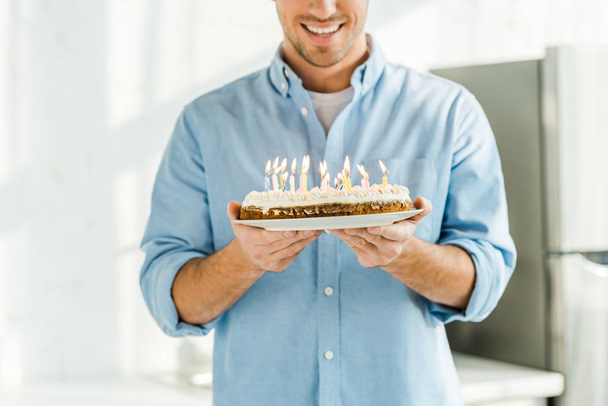 cropped view of smiling man holding birthday cake with burning candles at home in morning - Φωτογραφία, εικόνα