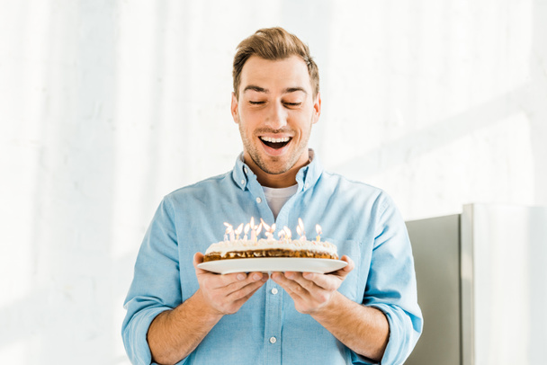 izgatott jóképű férfi születésnapi torta égő gyertyák otthon reggel gazdaság - Fotó, kép