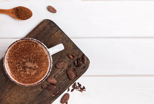 Hot chocolate in the cup, cocoa beans and powder on the white wooden table - Foto, Bild