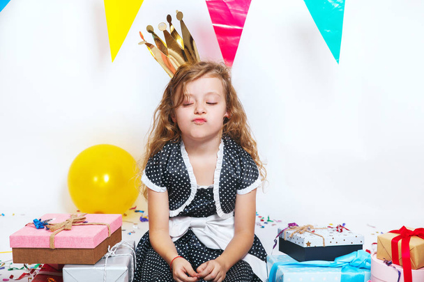 Portrait of an upset little girl in birthday hat with gifts - Foto, imagen