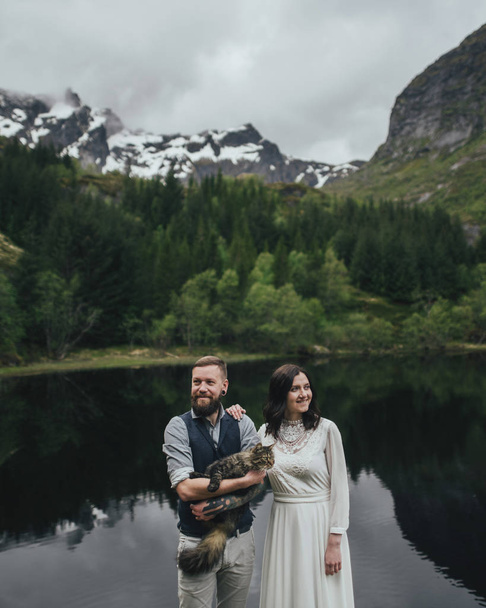 Portrait of young couple with cat with nordic mountains on background - Foto, immagini