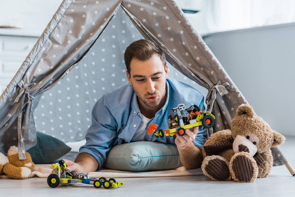 adult man lying in wigwam and playing with toys in nursery - Photo, Image