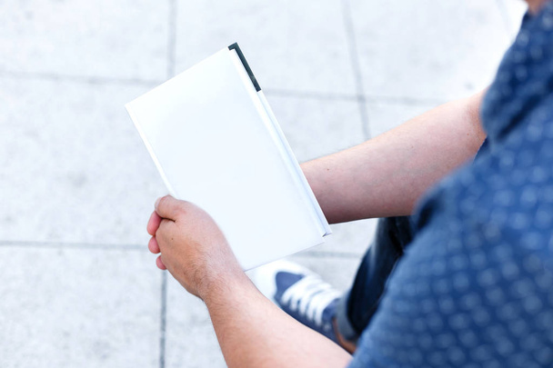 Man student  holds a closed white blank book outdoors. Hands clo - Фото, зображення