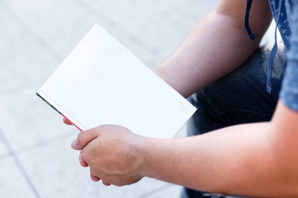 Male student holds a closed white blank book outdoors. Hands clo - Zdjęcie, obraz