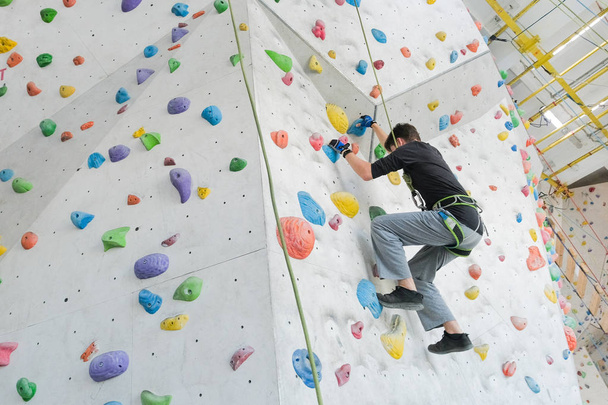 Sportsmen climbs boulder in a gym. A successful man climbing on climbing wall.                                         - Foto, immagini