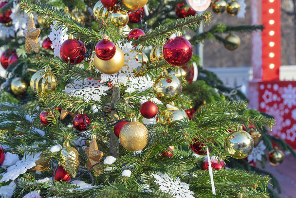A karácsonyfát díszített arany és piros golyó, és a fehér hópelyhek. - Fotó, kép