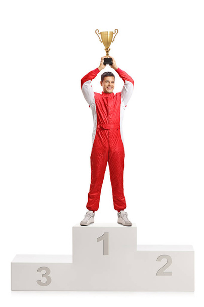 Full length portrait of a male car racer holding a gold trophy and standing on a winner's pedestal isolated on white background - 写真・画像
