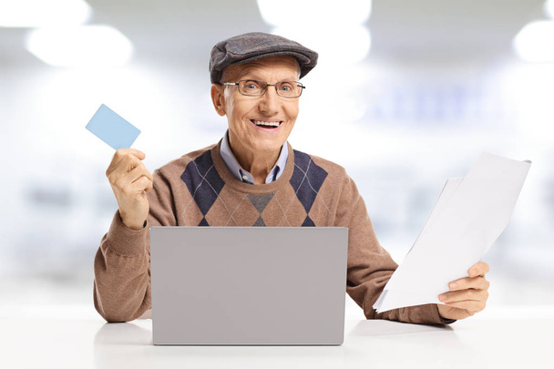 Smiling senior man paying bills with a credit card online on a laptop computer isolated on white background - Valokuva, kuva