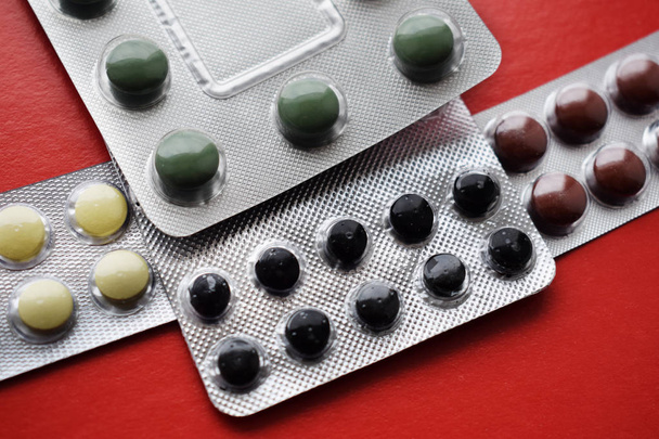 Différentes pilules et gélules colorées en boîtes - blisters. Médicaments pharmaceutiques destinés à être utilisés comme médicaments. Isolé sur un fond rouge
. - Photo, image