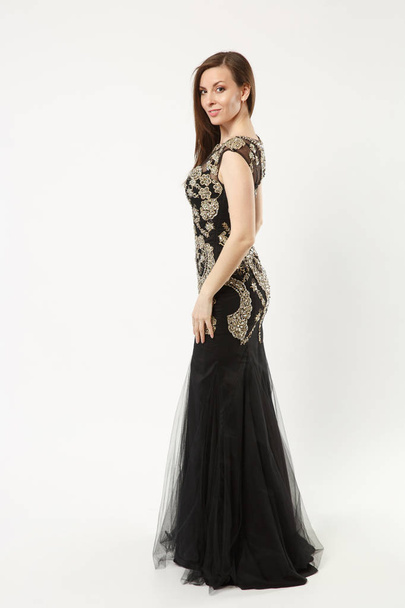 Full length photo fashion model woman wearing elegant evening dress black gown posing isolated on white wall background studio portrait. Brunette long hair girl. Mock up copy space. Side profile view. - Foto, afbeelding