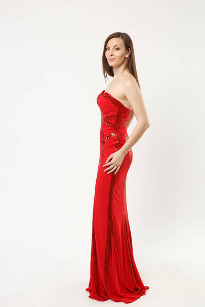 Full length photo fashion model woman wearing elegant evening dress red gown posing isolated on white wall background studio portrait. Brunette long hair girl. Mock up copy space. Side profile view. - Photo, Image