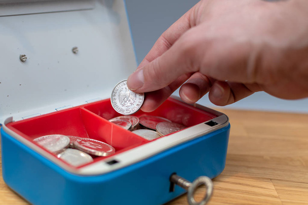 Hand legt eine Münze in eine blaue Kasse. - Foto, Bild