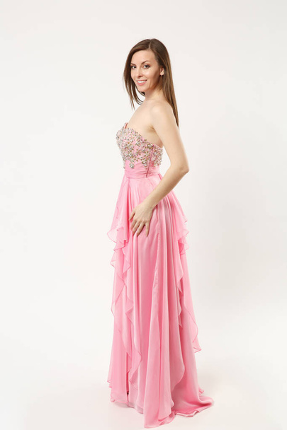 Full length photo fashion model woman wearing elegant evening dress pink gown posing isolated on white wall background studio portrait. Brunette long hair girl. Mock up copy space. Side profile view. - Photo, Image