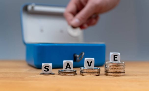 Dobbelstenen vorm het woord "save" op de top van stapels munten. In de rug - Foto, afbeelding