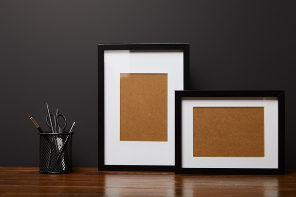 black square frames near metallic holder with stationery on wooden table  - Фото, изображение