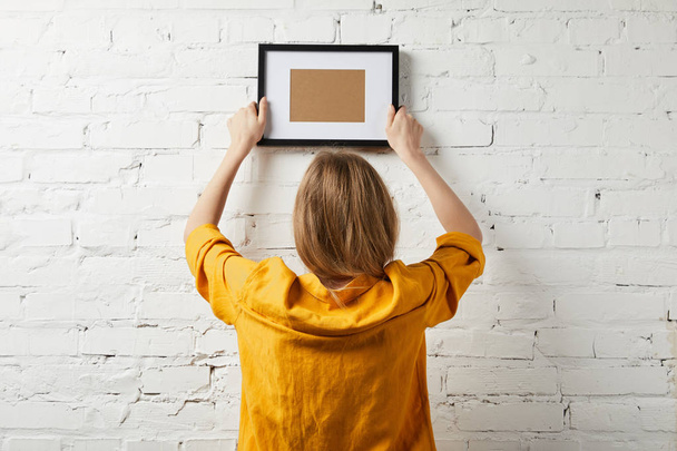 back view of woman holding blank black frame in hands - Foto, afbeelding