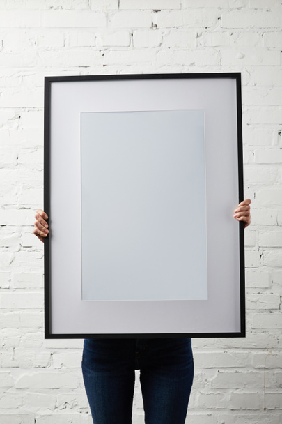 woman covering face while holding blank black frame in hands - Foto, Bild