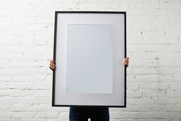 woman covering face while holding blank black frame  - Photo, Image