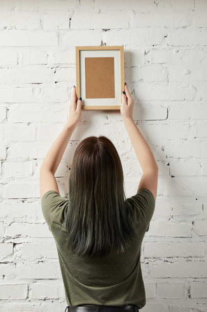 back view of woman holding blank brown square frame in hands - Fotó, kép