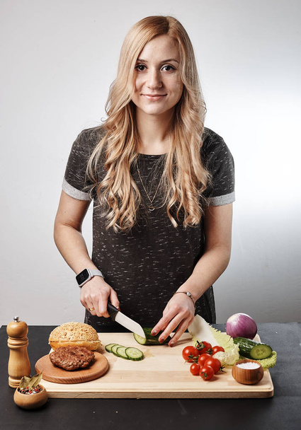 Blond smiling woman making burger at table - Foto, afbeelding