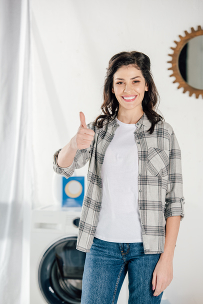 woman in grey shirt showing thumb up in laundry room - Fotoğraf, Görsel