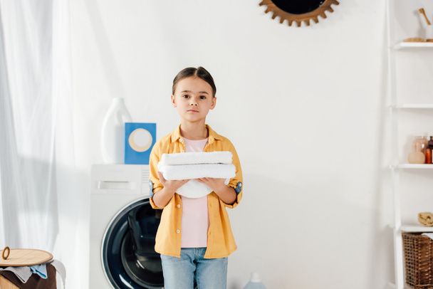 dziecko w żółte koszulki i jeansy gospodarstwa ręczniki w pralni - Zdjęcie, obraz