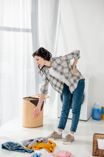 woman standing near baskets and holding backache in laundry room - 写真・画像