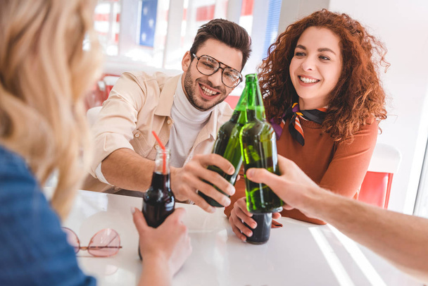 selective focus of handsome and beautiful friends cheering with glass bottles and smiling  - Foto, imagen
