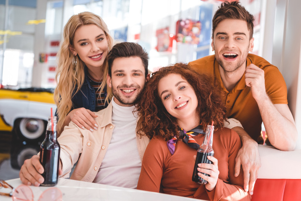 handsome and attractive friends holding glass bottles with soda and smiling  - Foto, Imagen