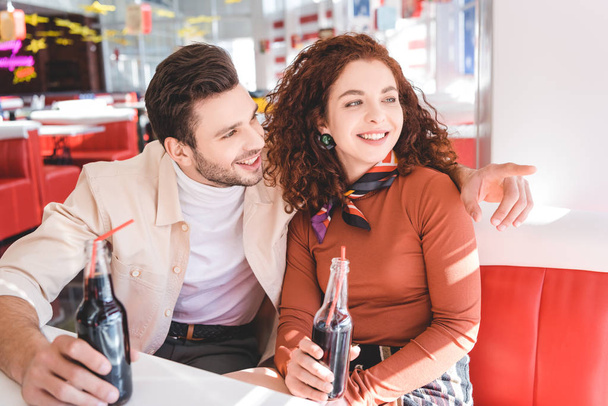 couple smiling, holding glass bottles with soda and looking away  - Foto, Imagem