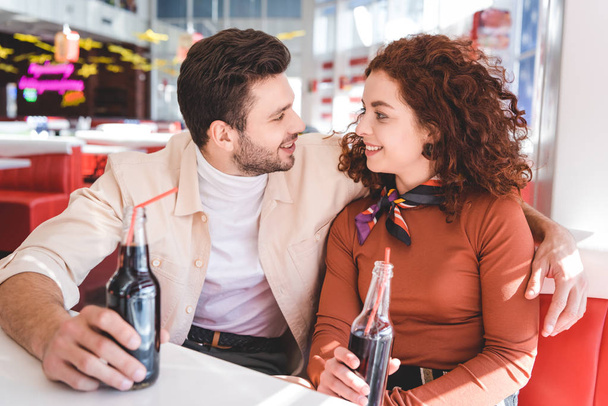pareja sonriendo, sosteniendo botellas de vidrio con soda y mirándose
  - Foto, Imagen