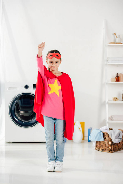 child in red homemade superhero suit in laundry room - Foto, afbeelding