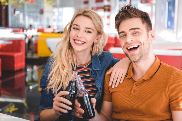 bella coppia sorridente, guardando la fotocamera e tifo con bottiglie di vetro al caffè
  - Foto, immagini