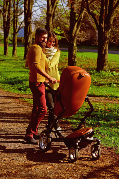 Woman and man parent push baby stroller while walking through autumn park, family bond. Happy family bond. Pleasure of togetherness - Photo, Image