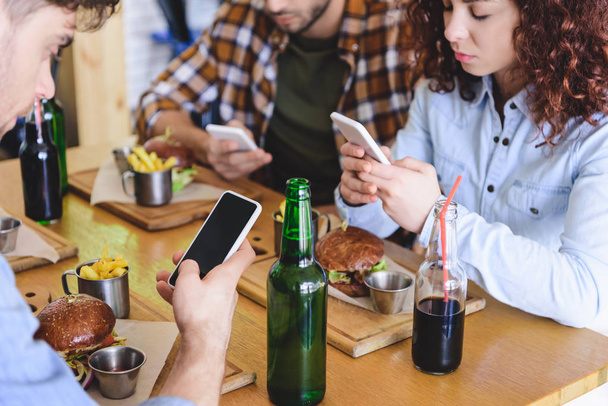 επιλεκτική εστίαση των φίλων χρησιμοποιώντας smartphones με αντίγραφο χώρου και κενή οθόνη στο café  - Φωτογραφία, εικόνα