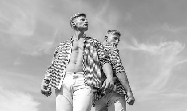 Menswear and fashion concept. Brothers twins looks attractive. Men strong athlete wear same shirts. Fashionable similar outfits. Men twins brothers muscular guys posing in shirts sky background - Photo, Image