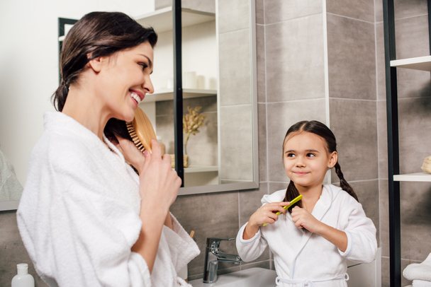 mother and daughter in white bathrobes combing in bathroom - Фото, зображення