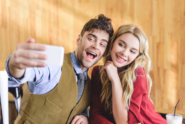 selective focus of beautiful and smiling couple taking selfie with smartphone at cafe  - Foto, immagini