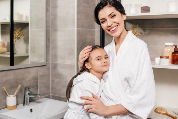 daughter and mother in white bathrobes hugging in bathroom - Fotoğraf, Görsel