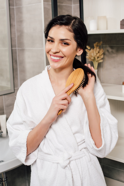Nainen valkoisessa kylpytakissa kampaus hiukset ja hymyilee kylpyhuoneessa
 - Valokuva, kuva