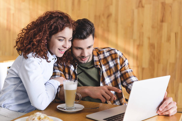 attractive woman and man hugging and using laptop at cafe  - Фото, зображення