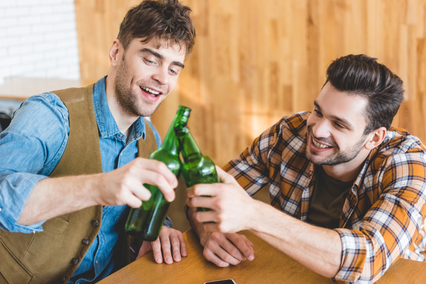 handsome and smiling men cheering with glass bottles of beer  - Фото, изображение
